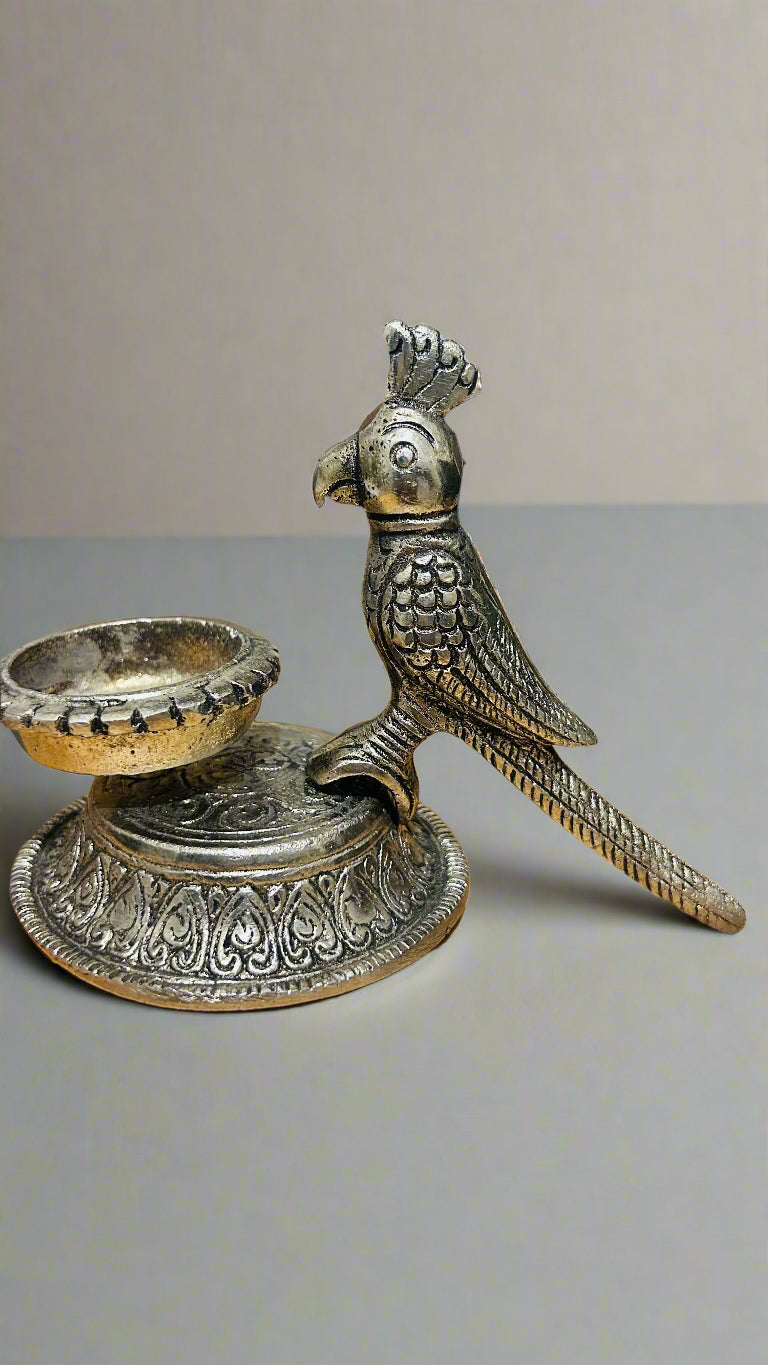 Decorative metal parrot figurine with a candle holder on a wooden surface.
