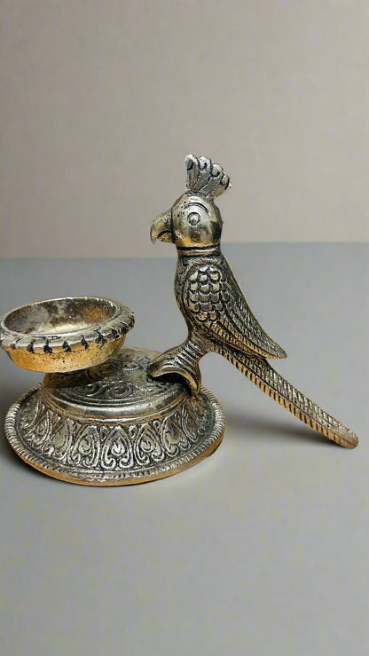 Decorative metal parrot figurine with a candle holder on a wooden surface.