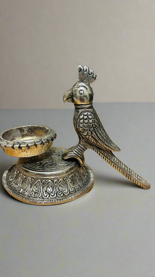 Decorative metal parrot figurine with a candle holder on a wooden surface.