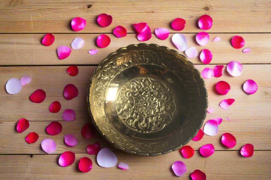 Decorative gold plate surrounded by pink and red rose petals on a wooden surface
